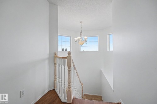 Staircase landing featuring a ceiling-mounted chandelier, white spindle railing, and wood-finish flooring - 262 Dunvegan Road, Edmonton, AB 