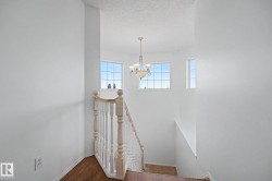 Staircase landing featuring a ceiling-mounted chandelier, white spindle railing, and wood-finish flooring - 