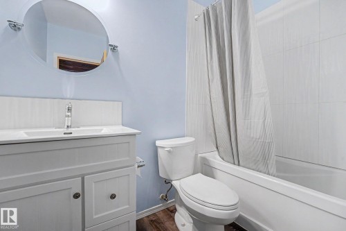 Bathroom featuring a white vanity with integrated sink, chrome faucet, and a circular mirror - 262 Dunvegan Road, Edmonton, AB 