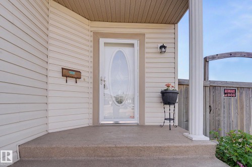 Inviting front entry featuring a white storm door with oval-shaped decorative glass, a porch light, and light-colored horizontal siding - 262 Dunvegan Road, Edmonton, AB 