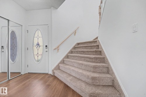 Entryway featuring wood-finish flooring, a white front door with an oval stained-glass insert, and sliding mirrored closet doors - 262 Dunvegan Road, Edmonton, AB 