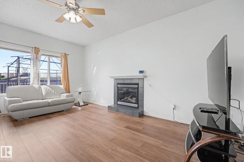 Living area featuring wood-finish flooring, a ceiling fan with integrated lighting, and a fireplace with a tiled surround and hearth - 262 Dunvegan Road, Edmonton, AB 