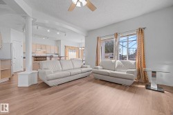 Spacious living area featuring wood-finish flooring, a ceiling fan, and architectural column detailing - 