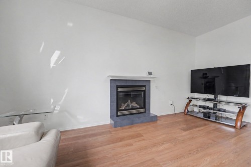 Living area featuring wood-finish flooring, a white textured ceiling, and a fireplace with a tiled surround and hearth - 262 Dunvegan Road, Edmonton, AB 
