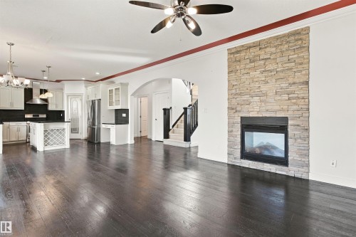 Dark wood-finish flooring, stone-clad fireplace with insert, white built-in cabinetry, stainless steel appliances, and a central island with a built-in wine rack - 1660 Malone Way Nw, Edmonton, AB 