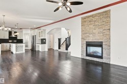 Dark wood-finish flooring, stone-clad fireplace with insert, white built-in cabinetry, stainless steel appliances, and a central island with a built-in wine rack - 