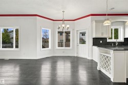 Dark wood-finish flooring, multiple windows, a white paneled door with glass insert, a chandelier, and white cabinetry with dark countertops - 