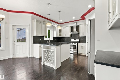 Spacious kitchen featuring dark wood-finish flooring, white cabinetry, dark countertops, a stainless steel range with overhead vent, and a central island with integrated wine storage - 1660 Malone Way Nw, Edmonton, AB 