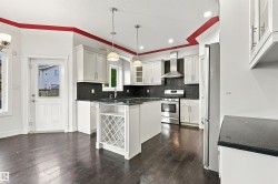 Spacious kitchen featuring dark wood-finish flooring, white cabinetry, dark countertops, a stainless steel range with overhead vent, and a central island with integrated wine storage - 