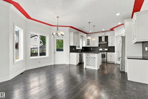 Expansive kitchen featuring white cabinetry, dark countertops, a center island with wine rack, stainless steel appliances, and dark wood-finish flooring - 1660 Malone Way Nw, Edmonton, AB 