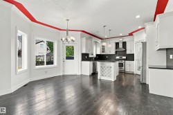 Expansive kitchen featuring white cabinetry, dark countertops, a center island with wine rack, stainless steel appliances, and dark wood-finish flooring - 
