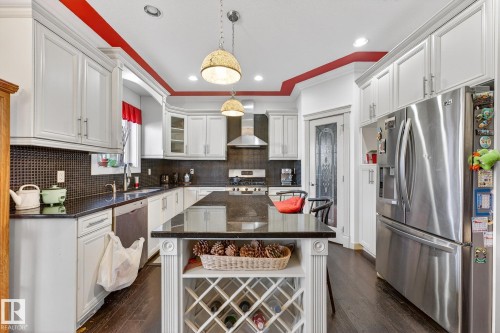 Kitchen featuring stainless steel appliances, dark stone countertops, dark wood-style floors, white cabinetry, and crown molding - 1660 Malone Way, Edmonton, AB 
