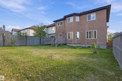 Expansive fenced backyard featuring a wooden deck, stucco exterior, and multiple windows - 1660 Malone Way Nw, Edmonton, AB 