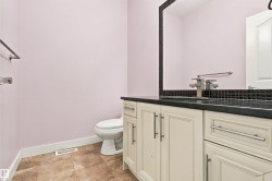 Cream-colored vanity cabinetry with brushed nickel hardware, dark countertop, and black tile backsplash - 