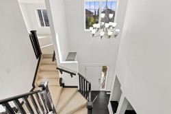 Two-story foyer featuring a prominent chandelier, upper-level transom windows, dark wood-finish handrails, and carpeted stairs - 