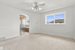 Light-colored carpet flooring, a ceiling fan with light fixture, a large window, an arched doorway, and an en-suite bathroom with a glass-enclosed shower and built-in tub - 