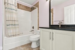 White vanity with brushed nickel hardware, a dark countertop, and a black mosaic tile backsplash - 