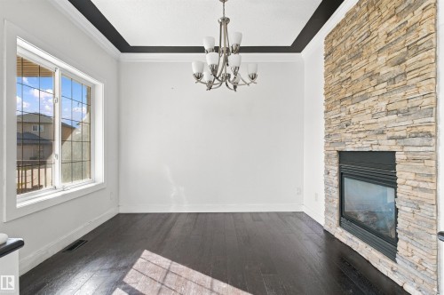 Dark wood-finish flooring, stone-clad fireplace, white crown molding, and recessed ceiling with a black accent - 1660 Malone Way Nw, Edmonton, AB 