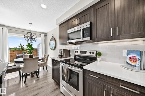 Modern kitchen featuring dark wood-finish cabinetry, stainless steel appliances, white subway tile backsplash, and light-toned countertops - 93 Richmond Link, Fort Saskatchewan, AB 