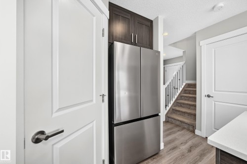 Stainless steel French door refrigerator integrated with dark wood-finish cabinetry - 93 Richmond Link, Fort Saskatchewan, AB 