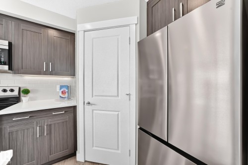 Modern kitchen featuring wood-finish cabinetry, stainless steel appliances, a white subway tile backsplash, and light-toned countertops - 93 Richmond Link, Fort Saskatchewan, AB 