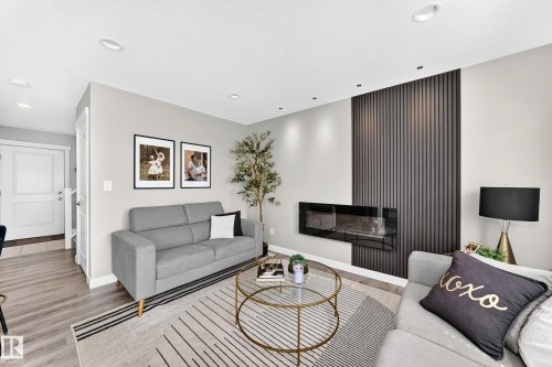 Living space with a contemporary linear fireplace, a dark vertical slat accent wall, recessed lighting, and wood-finish flooring - 93 Richmond Link, Fort Saskatchewan, AB 