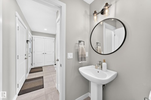 Pedestal sink with a round black-framed mirror, industrial-style vanity lighting, and light gray wall paint - 93 Richmond Link, Fort Saskatchewan, AB 