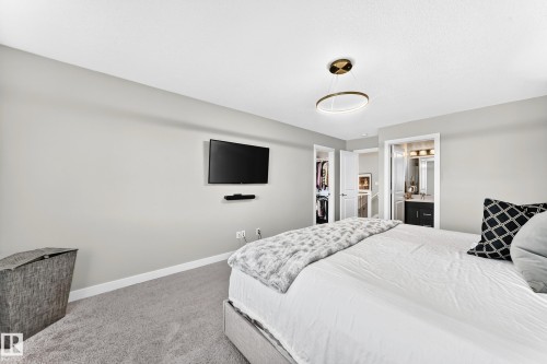 Carpeted bedroom featuring a contemporary circular chandelier, closet with bi-fold doors, and an en-suite bathroom with a dark wood-finish vanity - 93 Richmond Link, Fort Saskatchewan, AB 