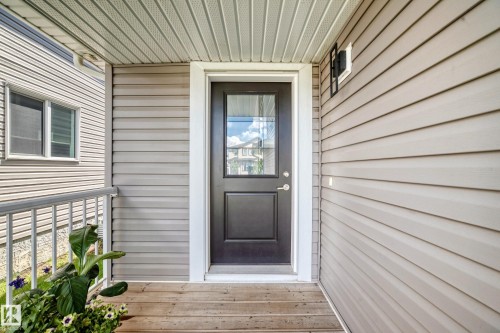 Covered porch entryway featuring a panel-style door with upper glass insert, light-toned horizontal siding, and a wood-finish porch floor - 93 Richmond Link, Fort Saskatchewan, AB 
