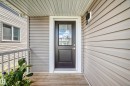 Covered porch entryway featuring a panel-style door with upper glass insert, light-toned horizontal siding, and a wood-finish porch floor - 93 Richmond Link, Fort Saskatchewan, AB 