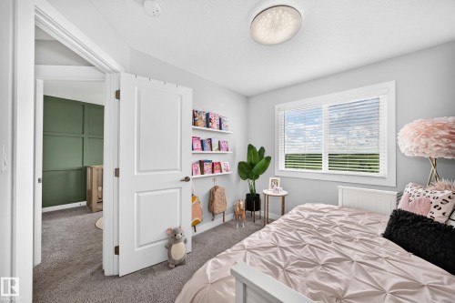 Spacious bedroom featuring light grey walls, a large window with white blinds, and a built-in shelving unit - 93 Richmond Link, Fort Saskatchewan, AB 