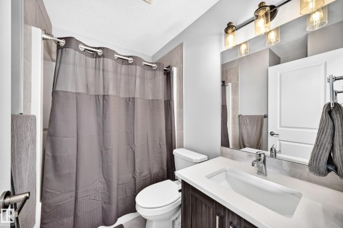 Bathroom featuring a modern vanity with integrated sink, chrome faucet, and wood-finish cabinetry - 93 Richmond Link, Fort Saskatchewan, AB 