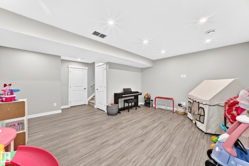 Spacious room featuring wood-finish flooring, recessed lighting, neutral grey wall paint, and white trim - 93 Richmond Link, Fort Saskatchewan, AB 