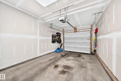 Attached garage featuring a concrete floor, an overhead door with opener, drywall walls, and a finished ceiling - 93 Richmond Link, Fort Saskatchewan, AB 