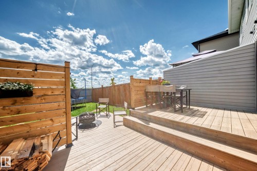 Multi-level wood deck featuring a privacy screen and direct access to a fenced yard with green space - 93 Richmond Link, Fort Saskatchewan, AB 