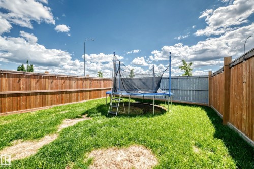 Grassed backyard area featuring a wood privacy fence and corrugated metal fencing - 93 Richmond Link, Fort Saskatchewan, AB 