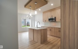 Modern kitchen featuring wood-finish cabinetry, a central island with integrated sink, and stainless steel microwave - 