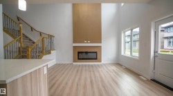 Great room featuring high ceilings, wood-finish flooring, a contemporary fireplace with a light-colored mantel, and a two-story accent wall - 