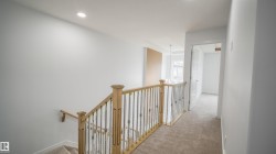 Upper-level hallway featuring light-colored carpeting, a light wood-finish banister with dark metal spindles, recessed ceiling lighting, and crisp white walls - 