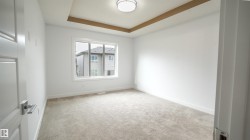 Recessed ceiling with wood-finish trim, large window, neutral carpeting, white walls, and a contemporary ceiling light fixture - 