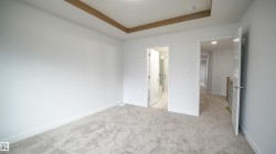 Carpeted room featuring a tray ceiling with wood-finish accents, white walls, and bright overhead lighting - 