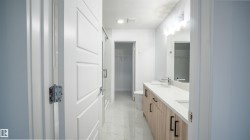 Spacious bathroom featuring a dual vanity with light wood-finish cabinetry, white countertops, and contemporary black pull handles - 