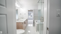 White-tiled bathroom featuring a dual vanity with light wood-finish cabinetry, a glass-enclosed shower, and a built-in bathtub - 