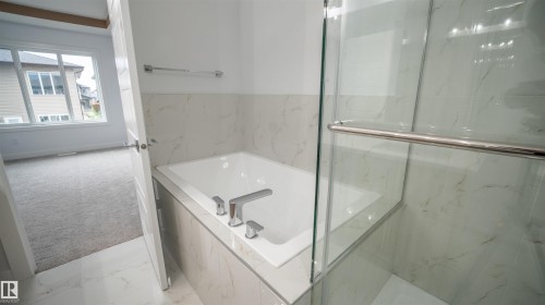 Bathroom featuring a built-in soaking tub with deck-mounted chrome fixtures, marble-finish wall and floor tile, and a glass-enclosed shower with chrome hardware - 3708 40 Ave, Beaumont, AB 