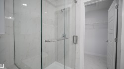 Glass-enclosed shower with white marble-style tile walls, a built-in bench, and polished chrome fixtures - 