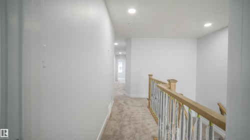 Upper-level hallway with neutral carpeting, recessed lighting, and a natural wood handrail with balusters - 3708 40 Ave, Beaumont, AB 