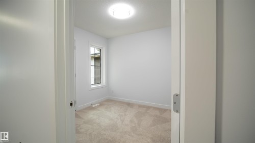 Carpeted interior room featuring a single window with blinds, baseboard trim, and a ceiling-mounted light fixture - 3708 40 Ave, Beaumont, AB 