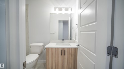 Bathroom featuring a light wood-finish vanity with a white countertop and rectangular sink, a wall-mounted mirror, and a three-light vanity fixture - 3708 40 Ave, Beaumont, AB 