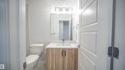 Bathroom featuring a light wood-finish vanity with a white countertop and rectangular sink, a wall-mounted mirror, and a three-light vanity fixture - 