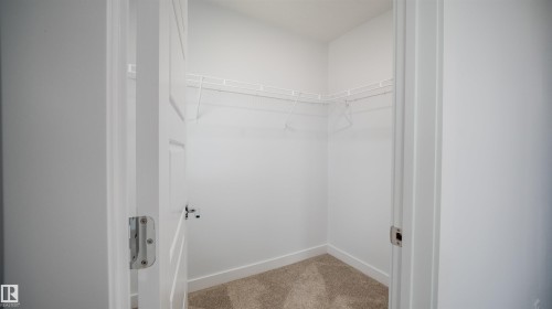 Walk-in closet featuring white wire shelving, light brown carpeting, white baseboards, and bright white walls - 3708 40 Ave, Beaumont, AB 